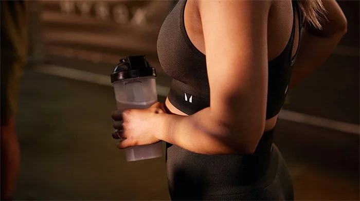 A close up of a young woman mid-exercise holding a Myprotein shaker.